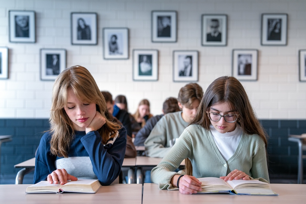 Leerlingen lezen elk een boek aan hun bureau in de klas.