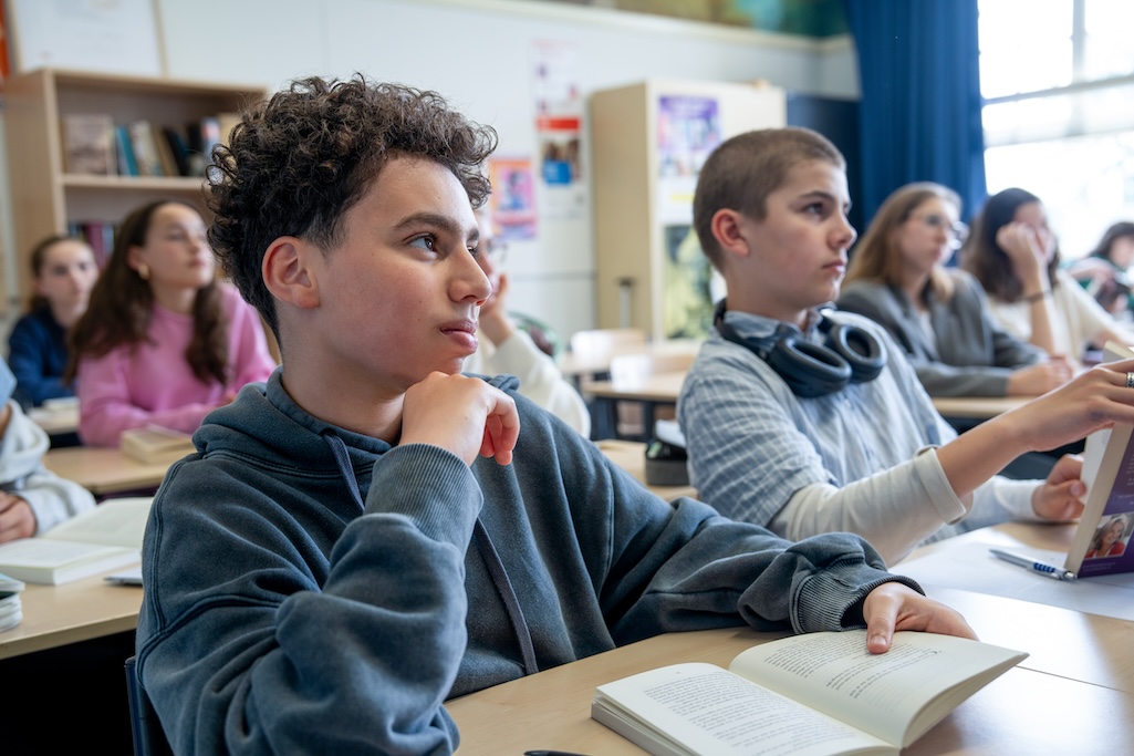 Leerlingen in de klas met een boek voor zich luisteren naar de docent